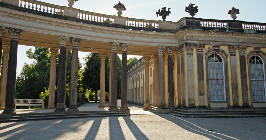 Sanssouci Palace courtyard in Potsdam, Germany, with a curved colonnade and sunlight across the historic facade.