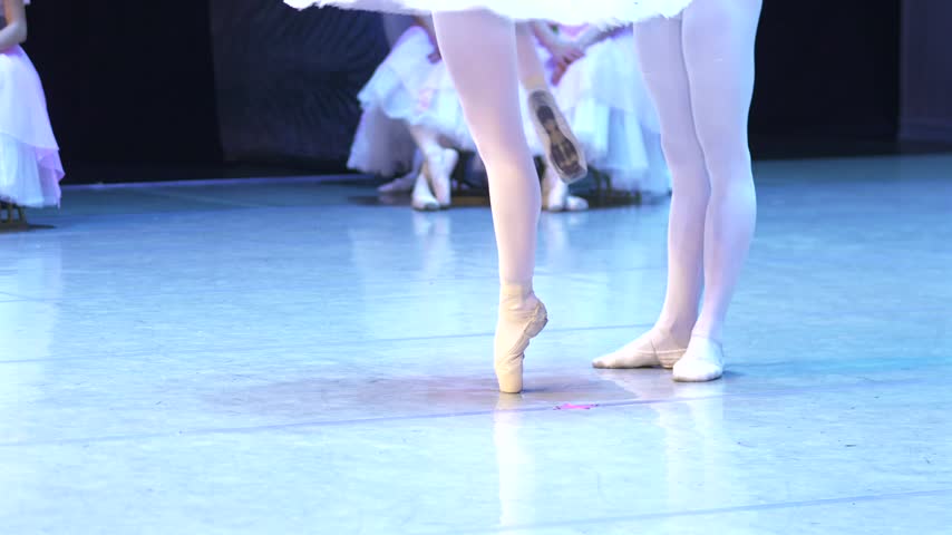 Close up of a ballerina on pointe with her partner performing an adagio from The Nutcracker on a blue-lit theater stage