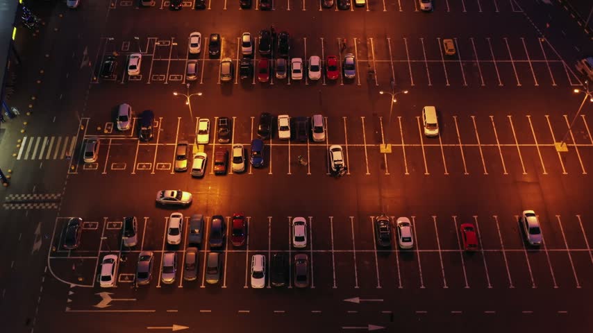 Aerial view of a parking lot at night with cars parked in marked spaces under bright streetlights in Russia.