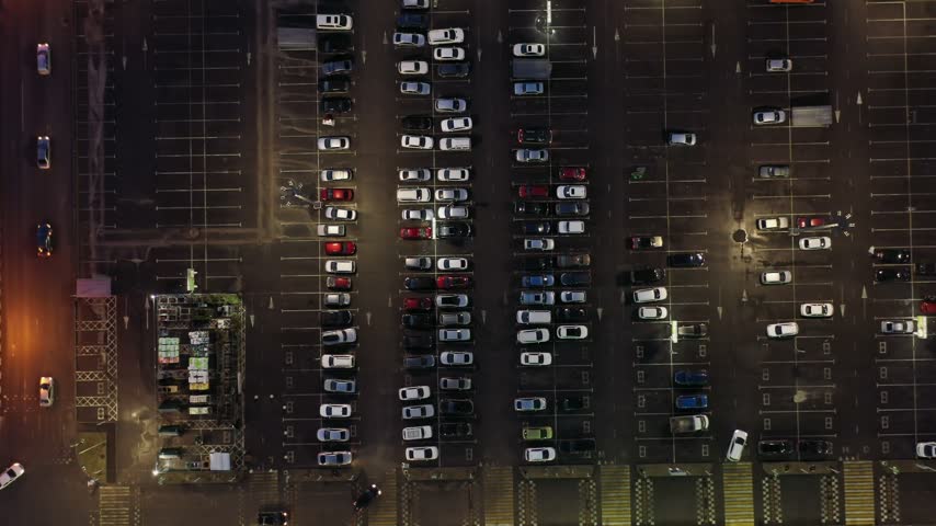 Aerial view of a parking lot at night with rows of parked cars illuminated by street lights in Russia.