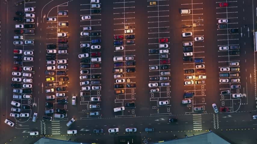 Aerial view of a large parking lot filled with numerous cars at dusk, illuminated by artificial lights in Russia.