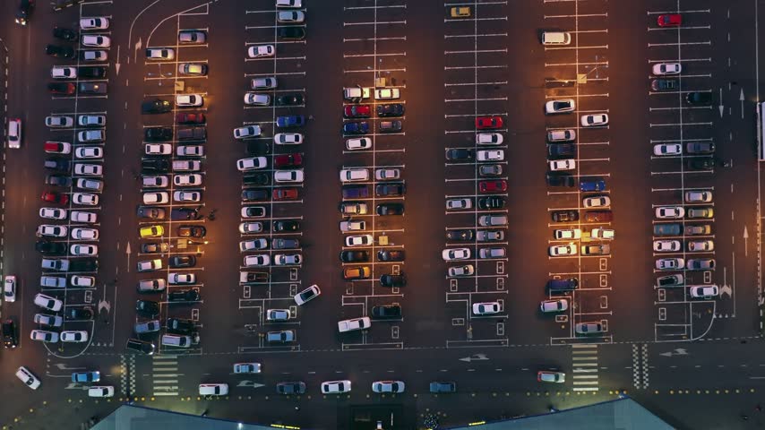 Aerial view of an illuminated parking lot with rows of parked cars on asphalt at night in Russia.