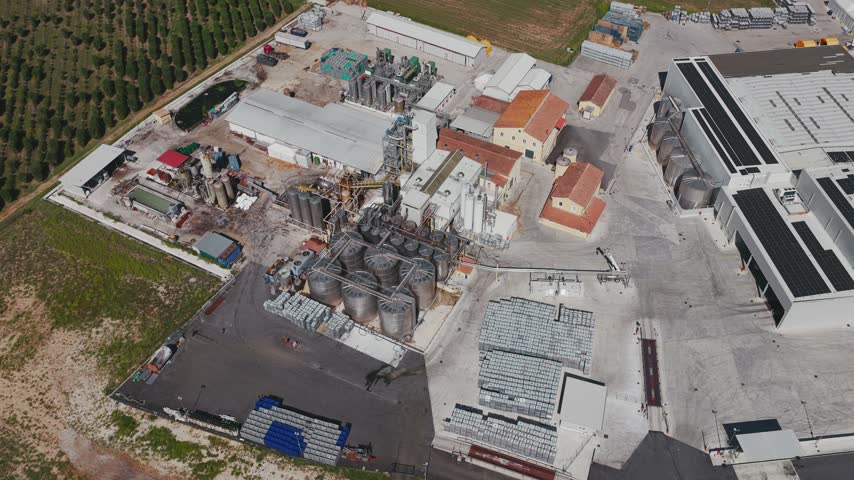 Aerial view of industrial facility with large stainless steel storage tanks and production buildings surrounded by agricultural fields in Spoleto, Umbria, Italy.