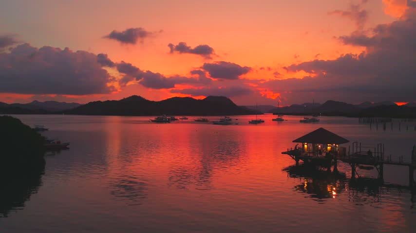 Vivid tropical sunset over Coron Bay with boats and a glowing pavilion reflected in calm water