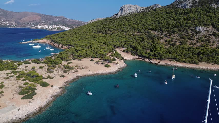 Aerial view of Moni Island bay near Aegina, Greece, featuring turquoise water, boats and a rugged Mediterranean coastline.