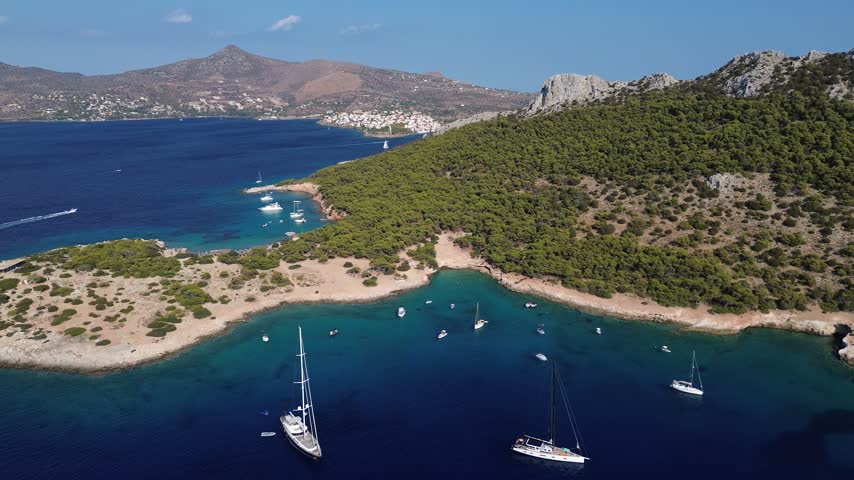 Aerial view of Moni Island bay near Aegina, Greece, featuring turquoise water, boats and a rugged Mediterranean coastline.