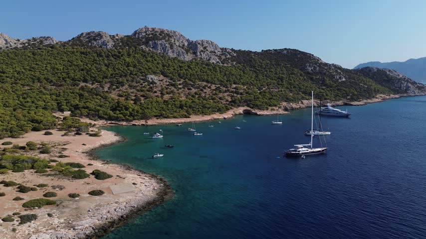 Aerial view of Moni Island bay near Aegina, Greece, featuring turquoise water, boats and a rugged Mediterranean coastline.