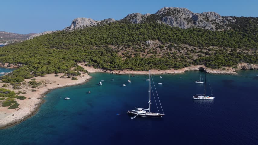 Aerial view of Moni Island bay near Aegina, Greece, featuring turquoise water, boats and a rugged Mediterranean coastline.