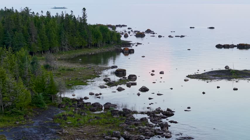 Aerial view approaches a remote forested inlet filled with scattered rocks and small islands in calm Lake Huron water.