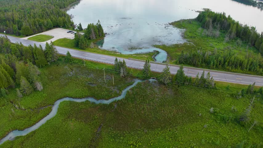 An aerial view reveals a paved road crossing winding wetland streams beside a forested bay near Hessel Michigan.