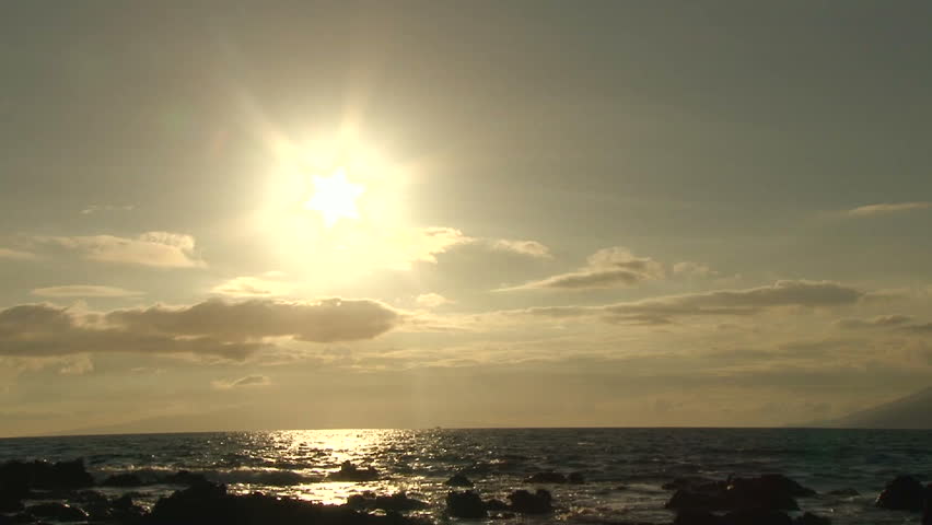 Sun shines over Pacific Ocean from beach in Hawaii with waves crashing.