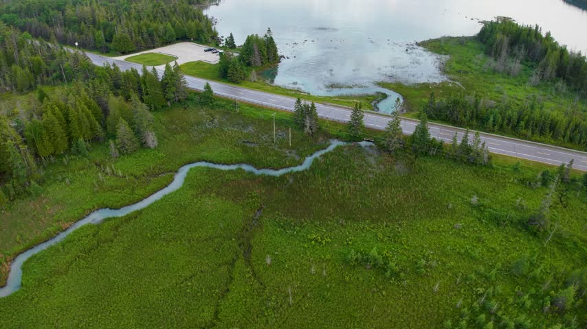 A winding creek snakes through lush green marshland below a coastal road and sheltered bay near Hessel Michigan.