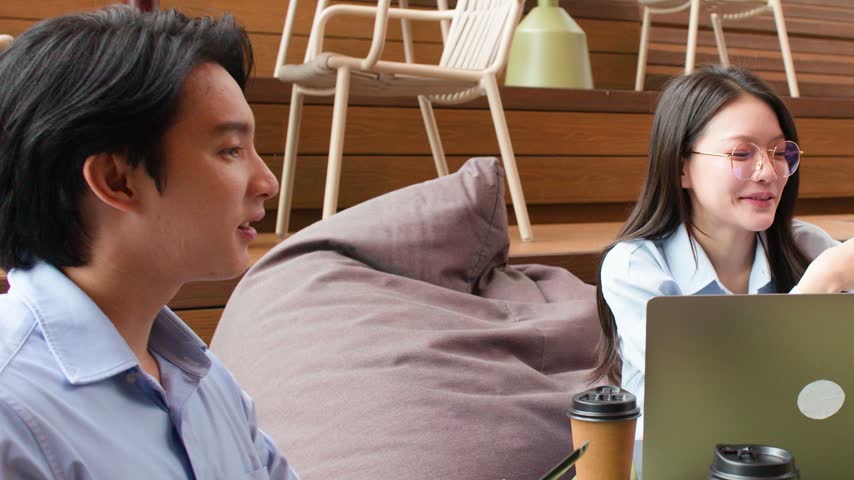 Young Asian professionals collaborate over a laptop in a contemporary office lounge setting.