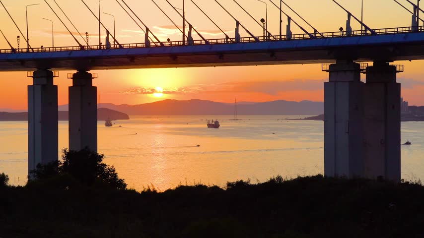 Beautiful sunset over Amur Bay and the Sea of Japan beneath Russky Bridge in Vladivostok, Russia, with glowing coastal scenery.
