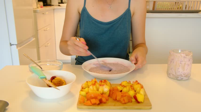 Young woman prepare tasty chia seed pudding with peaches and apricots at table, healthy eating habits