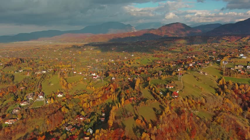 Aerial view of Transylvania autumn landscape with colorful trees, rolling hills, and scattered houses under a dramatic sky in Romania.