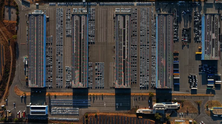 Aerial view of the automotive terminal at Civitavecchia Port with rows of new cars parked in large lots under bright sunlight in Civitavecchia, Lazio, Italy.