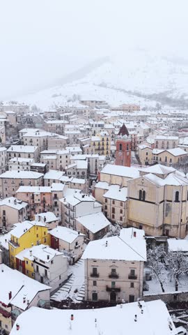 Aerial view of the snow-covered historic town of Rivisondoli with its traditional stone buildings and church tower under a winter sky in Rivisondoli, Abruzzo, Italy.