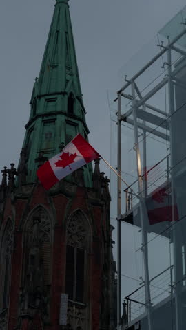 Historic church spire beside modern glass building with Canadian flag in urban skyline