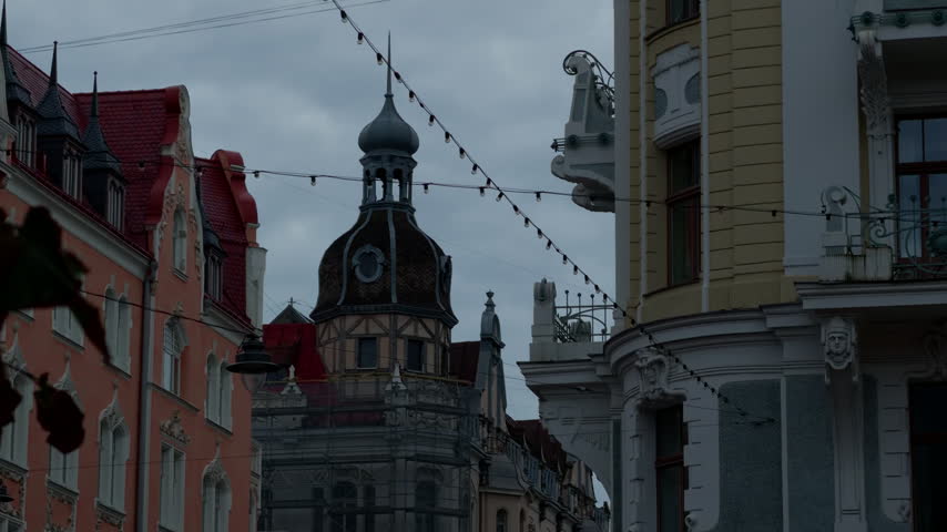 Ornate historic street with decorative facades, central turret, and hanging lights under cloudy sky