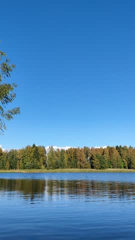 Panoramic view of calm blue lake under bright sunny sky with light clouds and shoreline.