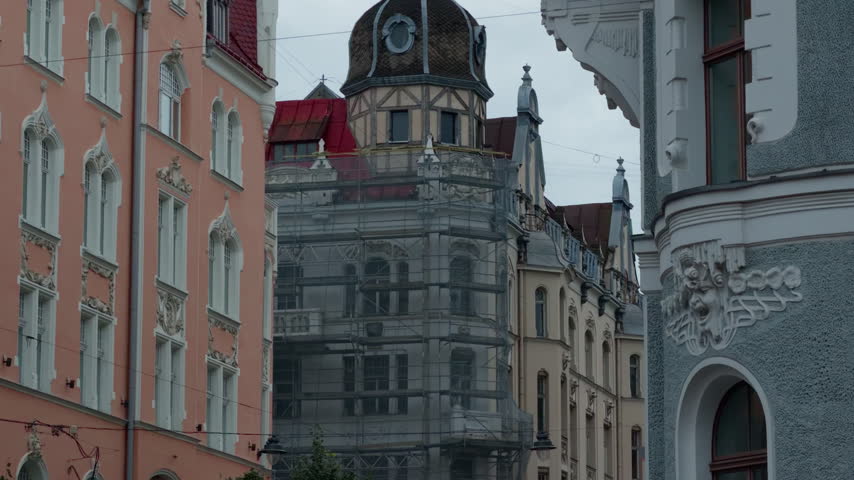 Ornate historic city street with pastel facades and scaffolded building under cloudy sky