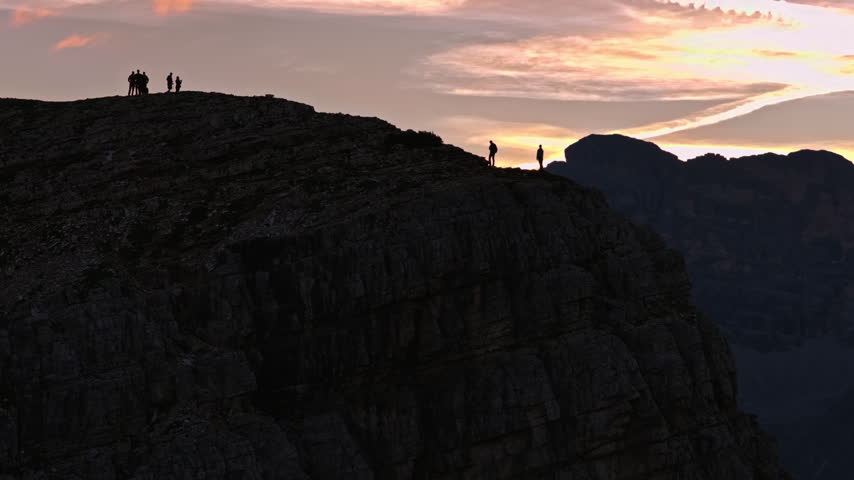 Silhouetted Hikers Stand On A Steep Rocky Mountain Ridge Watching The Sunrise Sky Over Cadini Di Misurina In The Italian Dolomites. - wide shot