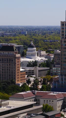 Aerial tracking view reveals California State Capitol dome past downtown office buildings and government headquarters in Sacramento on a clear sunny day.