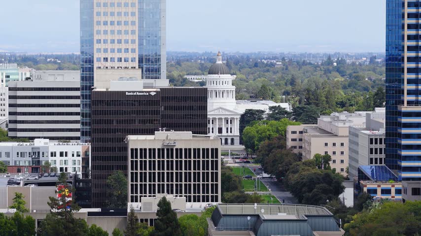 Aerial view of the California State Capitol building surrounded by city skyscrapers and tree lined avenues in downtown Sacramento, California, on a clear day.