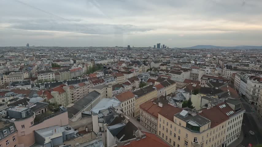 Aerial view across the historic urban landscape of Vienna, Austria, showing dense city blocks, rooftops and modern towers in the distance.