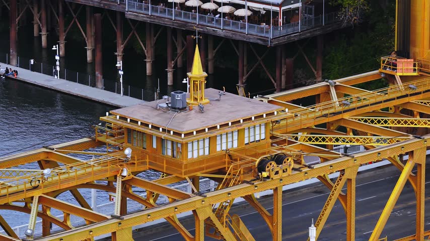 Aerial view shows the yellow steel structure and operator cabin of the historic Tower Bridge over the Sacramento River in Sacramento, California, with roadway traffic below.