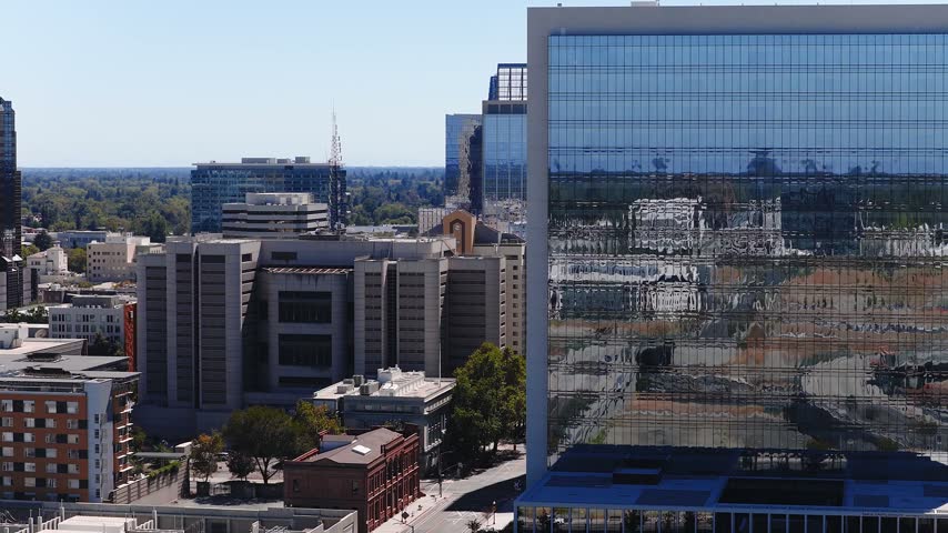 Aerial view gliding over downtown Sacramento California showing modern glass office skyscrapers, streets, and urban government architecture under bright clear daylight.