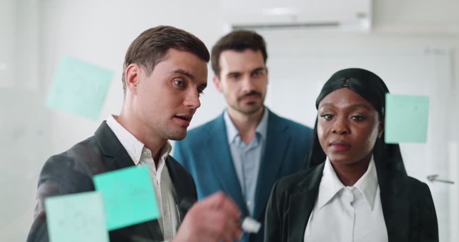 Portrait of multiracial business professionals plan on marketing strategy in office. Manager writes important task for team on glass board in coworking