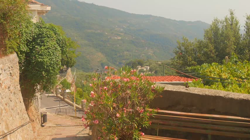 Wooden Bench And Potted Flowering Plants Overlook A Scenic Mountain Valley Path In The Medieval Village Of Perinaldo In Liguria, Italy.