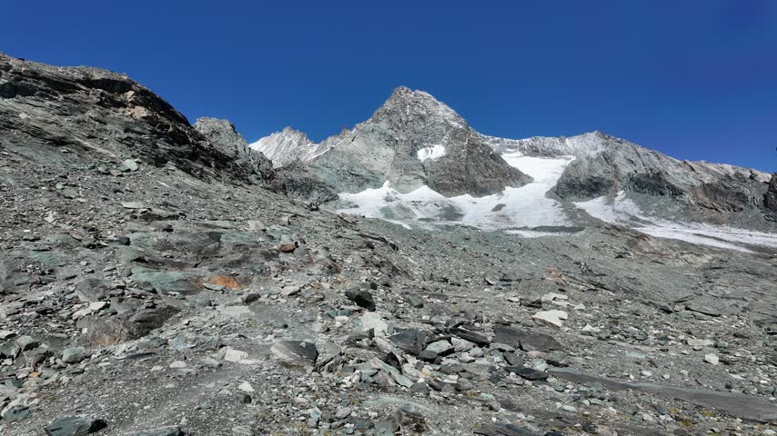 View of Grossglockner from near Studl Hut in the Austrian Alps, dramatic glaciated mountain landscape with hikers on a rocky ridge beneath clouds and blue sky