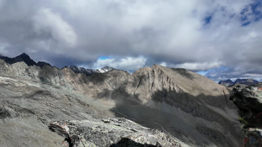 View of Grossglockner from near Studl Hut in the Austrian Alps, dramatic glaciated mountain landscape with hikers on a rocky ridge beneath clouds and blue sky