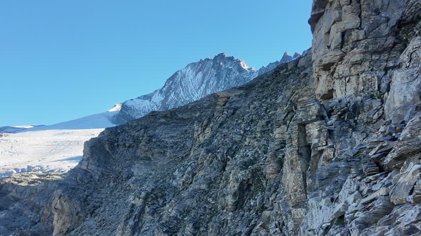 View of Grossglockner from near Studl Hut in the Austrian Alps, dramatic glaciated mountain landscape with hikers on a rocky ridge beneath clouds and blue sky
