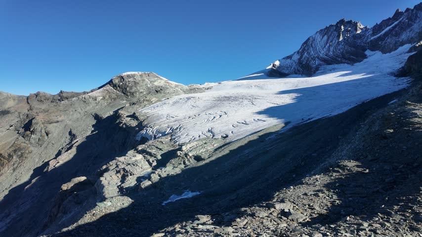 View of Grossglockner from near Studl Hut in the Austrian Alps, dramatic glaciated mountain landscape with hikers on a rocky ridge beneath clouds and blue sky