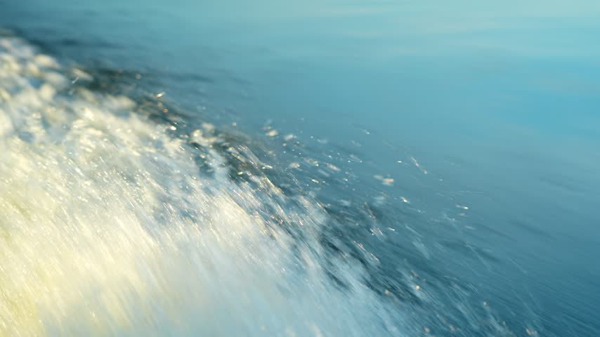 The motorboat is sailing across the surface of the lake, leaving a foamy trail behind it. Close‑up of the splashes. Active outdoor recreation.