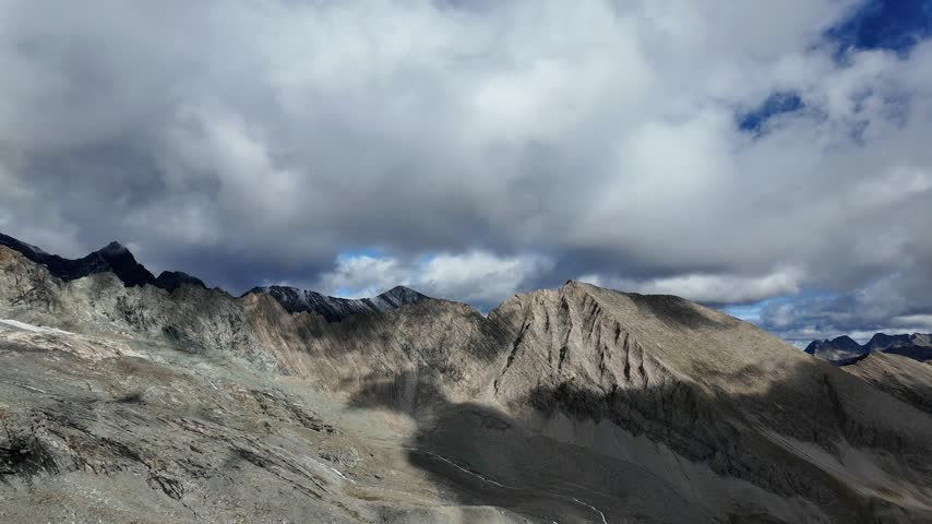 View of Grossglockner from near Studl Hut in the Austrian Alps, dramatic glaciated mountain landscape with hikers on a rocky ridge beneath clouds and blue sky