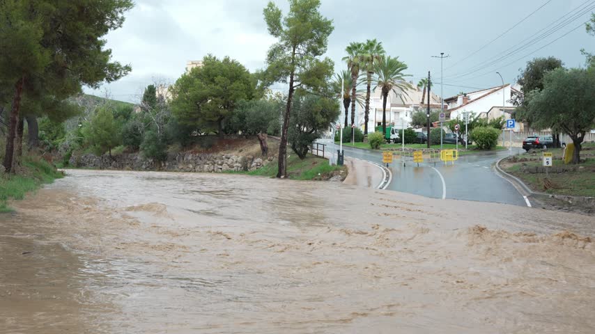 Muddy river water from a flash flood overflowing its banks and covering a road in sant pere de ribes