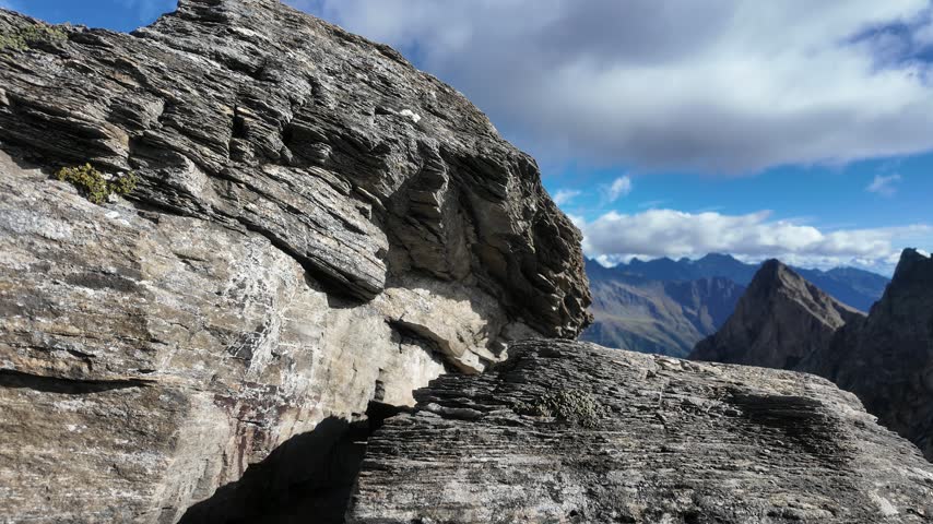 View of Grossglockner from near Studl Hut in the Austrian Alps, dramatic glaciated mountain landscape with hikers on a rocky ridge beneath clouds and blue sky