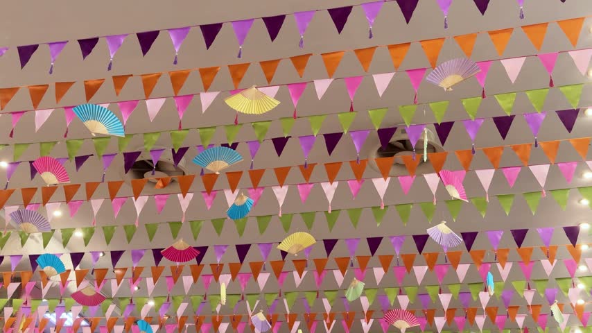 Large indoor hall with a ceiling decorated with colorful pennant flags and small paper fans for a festive event.