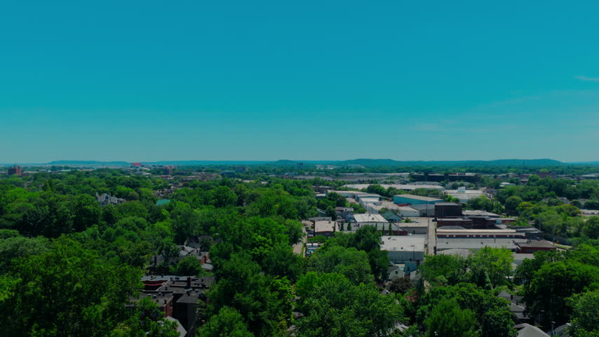 Louisville, Kentucky landscape. The footage highlights vast green tree canopies, scattered local businesses, and rolling distant hills under a vibrant blue sky. Midwest and Southern travel content