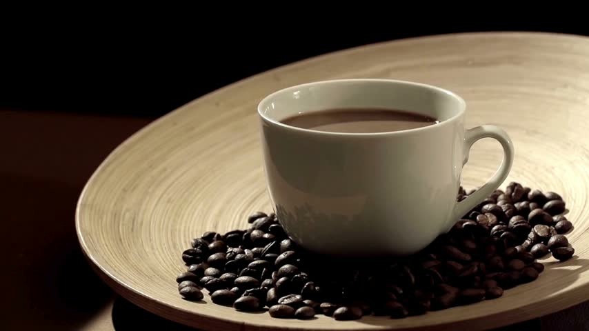 sugar cube fall on Coffee cup filled with dark liquid sits on a wooden plate. Roasted coffee beans scatter around the plate creating a rich, inviting display that highlights coffee culture.