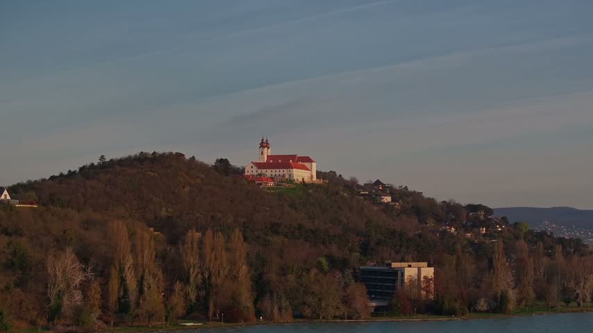 Aerial view of historic Tihany Abbey standing on a wooded hill above Lake Balaton, Hungary, illuminated by warm evening light and surrounded by scenic countrysid