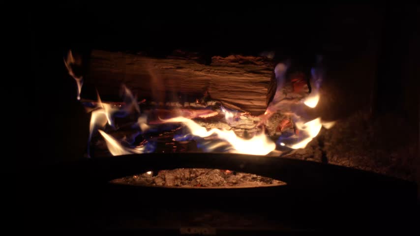 Logs burn with bright flames inside a fireplace, casting a warm indoor glow.