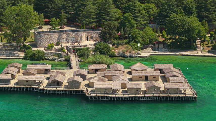 Aerial view shows reconstructed prehistoric wooden dwellings above Lake Ohrid beside a stone fort in North Macedonia.