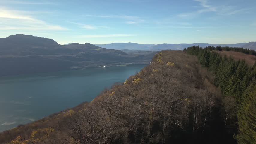 Cinematic drone orbit over Lake Bourget, Corsuet Forest and the surrounding French Alps on a sunny day, showcasing a scenic mountain landscape in Savoie, France.