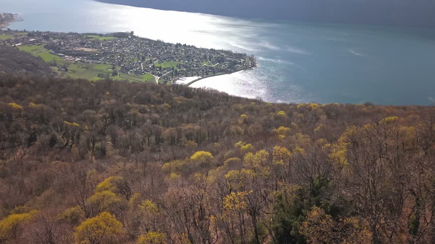 Drone tilt-up over Aix-les-Bains and Lake Bourget in the French Alps, revealing Dent du Chat, surrounding mountains and valley beneath a sunny sky with scattered clouds.